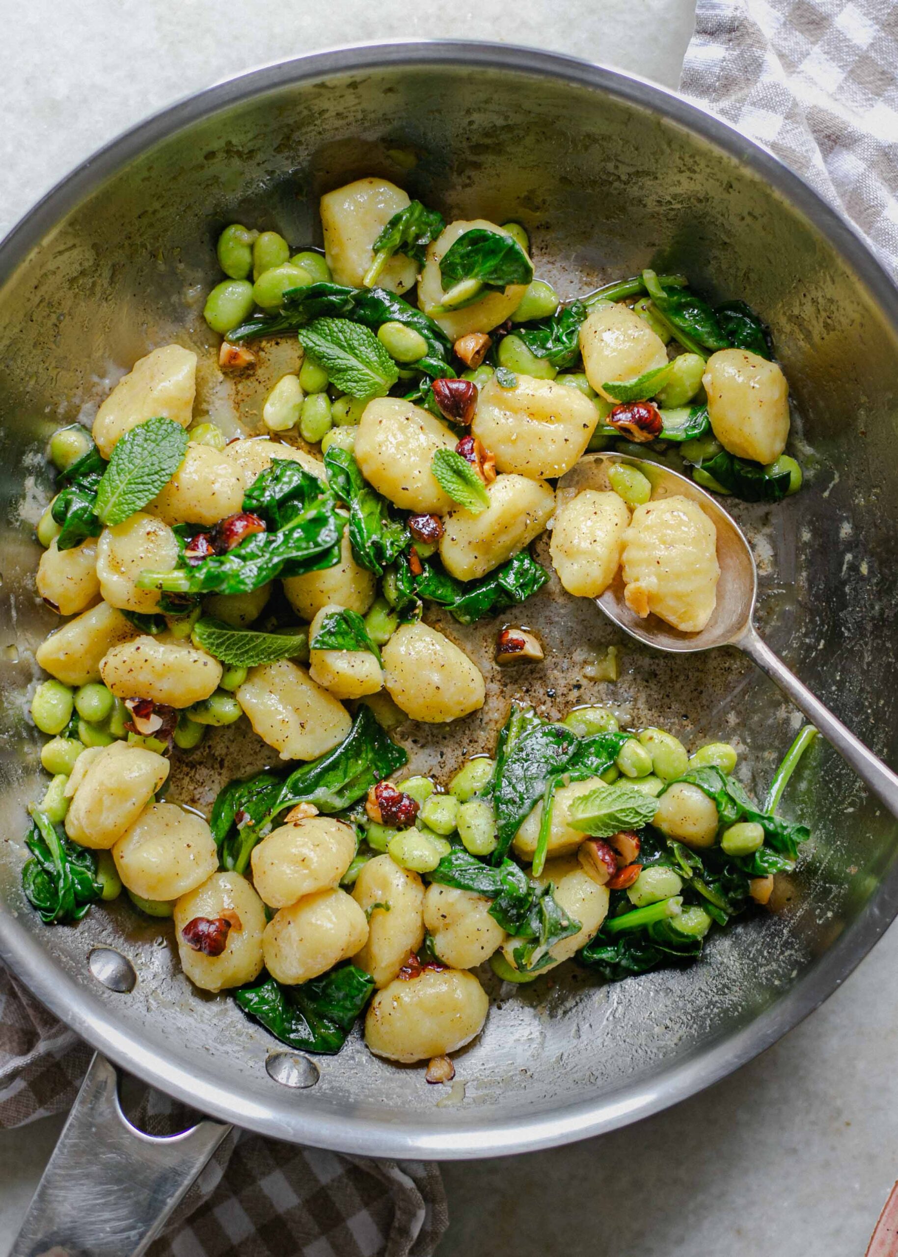 A frying pan of gluten free gnocchi with brown butter, spinach, sprinkled with hazelnuts also low FODMAP
